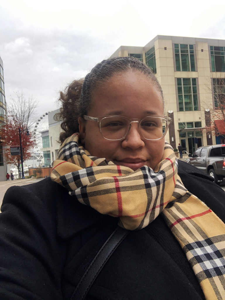 Ashley a.k.a girlwithherviews in maryland during wintertime. Wearing a black trench coat and a tan burberry scarf and her signature transparent glasses