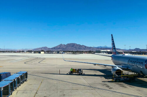 Image of American Airlines Plane on the tarmac parked at a gate, with a view of the mountains behind it.