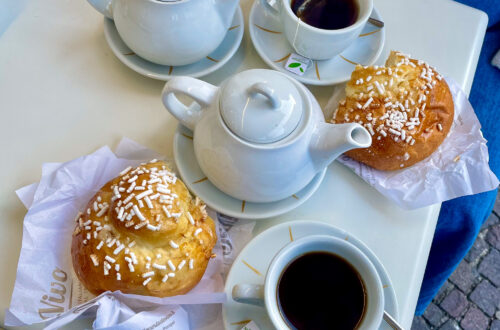 An Italian Breakfast of sugar covered broiche buns with two teapots and two teacups filled with black tea